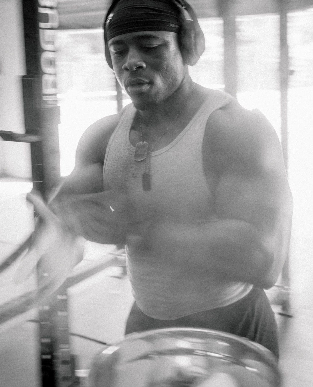 A person wearing headphones and a tank top working out, with a focused expression in a gym.