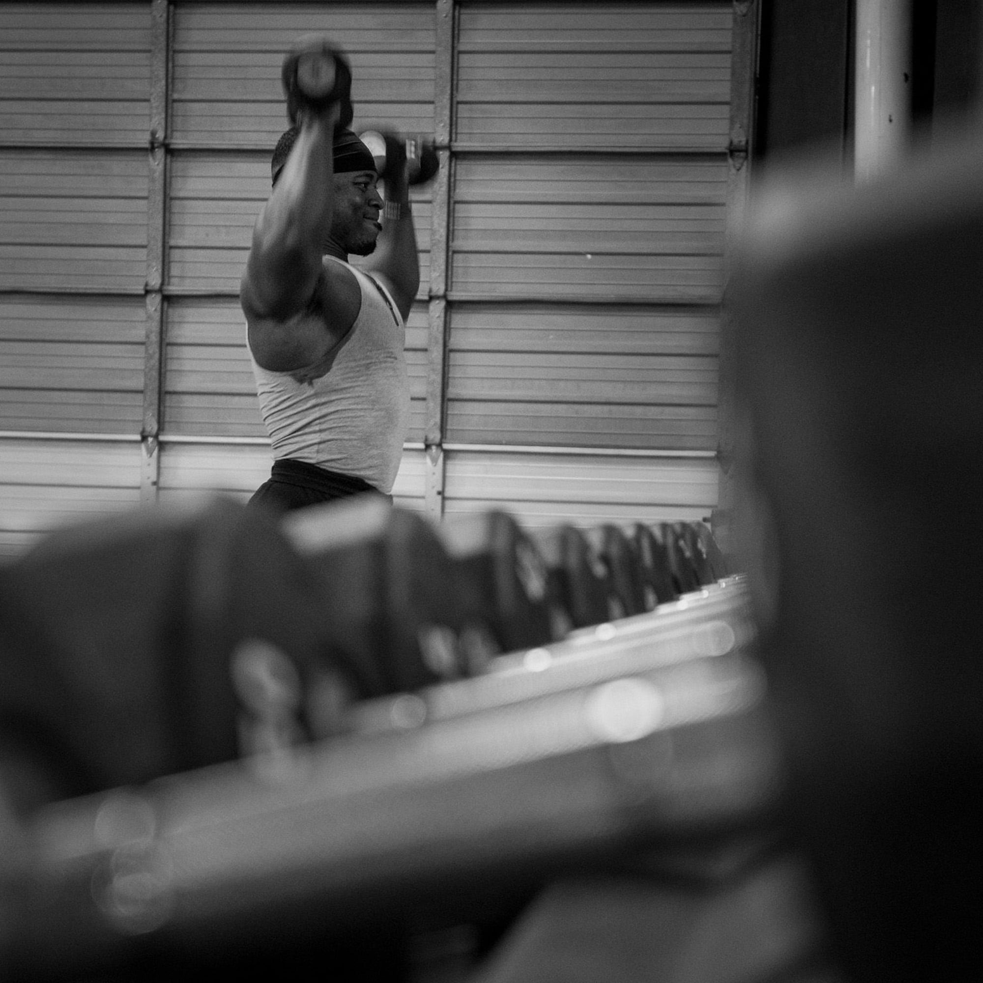A man lifting dumbbells at the gym near a rack of weights.