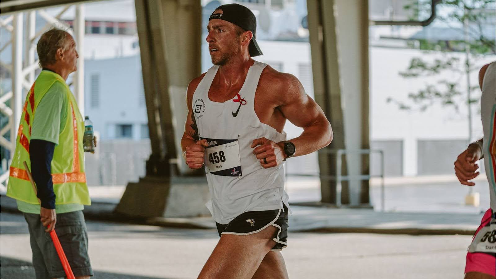 A runner in athletic gear participates in a marathon event under a roadway bridge.
